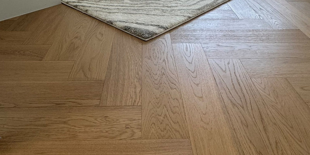 Light oak herringbone floor laid by Adore, with the corner of a textured rug