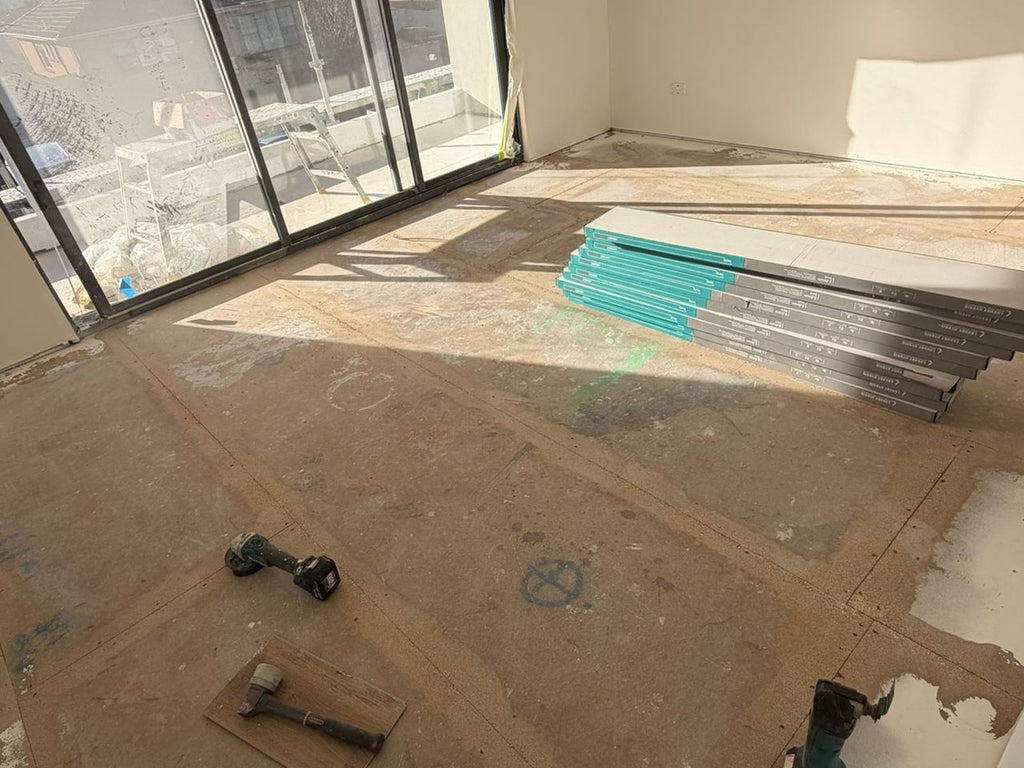 Living room stripped back to the subfloor, with flooring packs and tools ready for installation