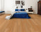 A warm orange-tan hybrid plank floor with a light amber tone in a bedroom with a blue bedspread