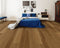A mid to dark brown hybrid plank floor ranging from honey to dark brown in a bedroom with a blue bedspread