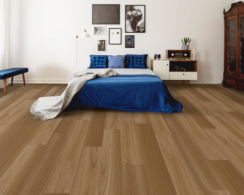 A mid golden brown hybrid plank floor with board variation in a bedroom with a blue bedspread