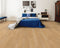 A light warm honey-tan hybrid plank floor in a bedroom with a blue bedspread