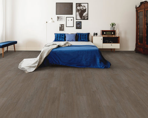 A mid to dark charcoal grey hybrid plank floor in a bedroom with a blue bedspread