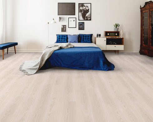 A very pale off-white hybrid plank floor with a whitewashed look in a bedroom with a blue bedspread